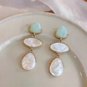 Elegant three-tier resin dangling earrings with pearlescent finish and gold-tone trim detail