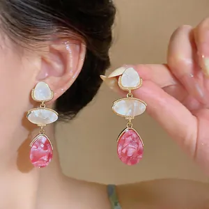 Close-up view of elegant pink and white resin drop earrings with gold-tone frames on model.