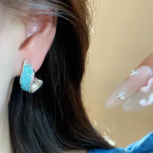 Close-up of irregular twisted silver needle earrings with blue glass inlay on a model's ear.