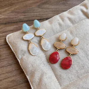 Close-up of vibrant resin teardrop tassel earrings displayed on a soft fabric pouch