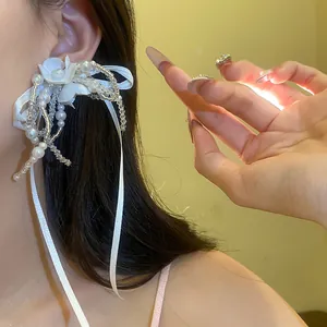Detail view of handmade white flower earring with elegant pearl tassels and long ribbons