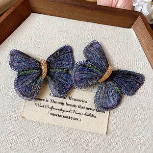Detailed view of elegant blue and purple embroidered butterfly hair clips on a wooden tray