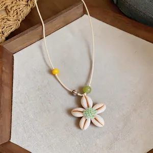 Dettaglio di un ciondolo a fiore in resina con centro di perline verdi su corda beige.