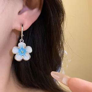 Elegante primo piano di orecchini a fiore in smalto blu e bianco su un orecchio.