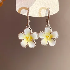 Dettaglio di eleganti orecchini a sospensione con fiori di frangipane bianco e ganci.