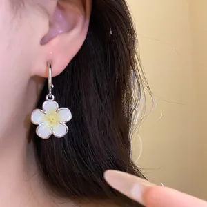Primo piano di un orecchino con ciondolo a fiore in smalto argentato indossato sull'orecchio.