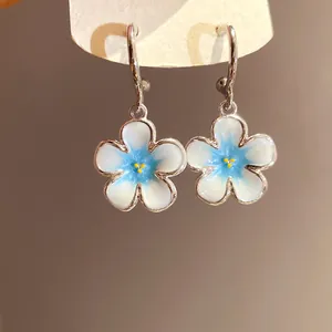Primo piano di raffinati orecchini a cerchio a C con fiori smaltati bianchi e blu.