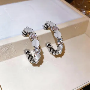 Close-up of elegant C-shaped earrings with cat eye stones and sparkling zircons