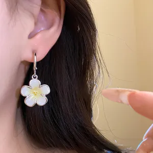 Dettaglio ravvicinato di un orecchino a fiore in smalto bianco indossato all'orecchio