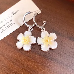 Dettaglio macro di orecchini a cerchio a C in argento con pendenti a fiore in smalto bianco