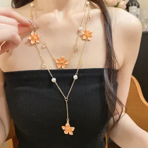 Detailed view of a layered gold necklace featuring orange flower pendants and elegant faux pearls