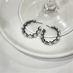 Detailed view of gunmetal hoop earrings with clear zircons and white cat's eye stones.