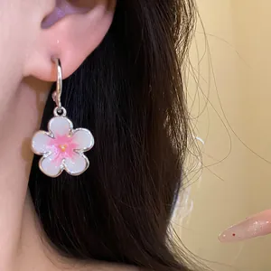 Dettaglio ravvicinato di un orecchino a fiore bianco e rosa indossato da una modella, gioielli