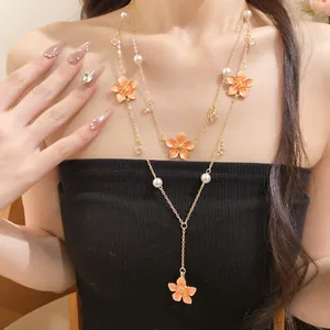 Detail of layered gold chain necklace featuring orange enamel flowers and faux pearls.