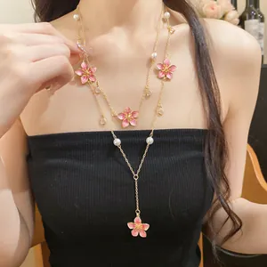 Close-up of a layered Y-shaped necklace featuring pink enamel flowers and faux pearls