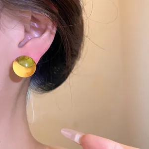 Elegant round yellow resin stud earrings with silver needles on ear, sunset style photography