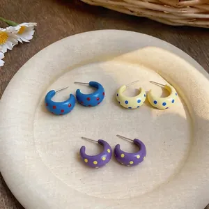 Pendientes de aro en forma de C con lunares de colores sobre una bandeja blanca