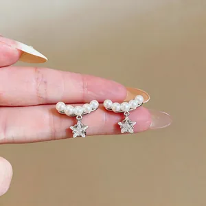 Gros plan sur d'élégantes boucles d'oreilles clips étoile et perle sur les doigts