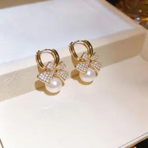 Close-up of elegant gold-plated bow earrings with sparkling zircons and pearls