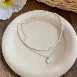 Detalle de collar de perlas de dos capas con colgante cuadrado en plato beige