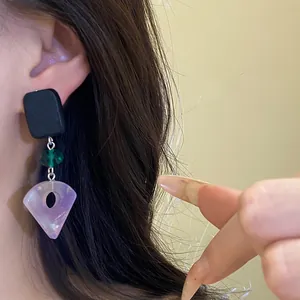 Close-up of minimalist square wood and purple resin fan pendant earring worn on ear.