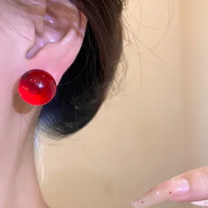 Close-up view of a vibrant red translucent resin round stud earring worn on the ear