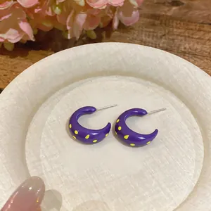 Primer plano de aretes de aro de esmalte morado en forma de C con lunares amarillos