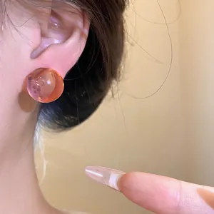 Detail view of a stylish translucent orange resin round stud earring worn on the ear