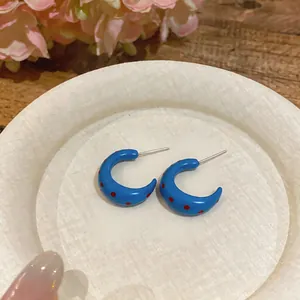 Vista detallada de pendientes de esmalte azul en forma de C con motivo de lunares rojos