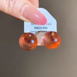 Close-up of amber resin round stud earrings with silver pins on a white tag