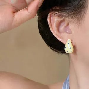 Primer plano de pendiente de esmalte amarillo con lunares azules en oreja