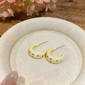 Detalle de pendientes amarillos en forma de C con lunares azules y acabado esmaltado