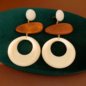 Macro detail view of geometric wood and resin drop earrings displayed on green velvet