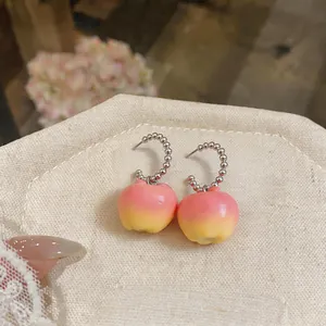 Gros plan sur des boucles d'oreilles pomme en résine avec dégradé rose et jaune