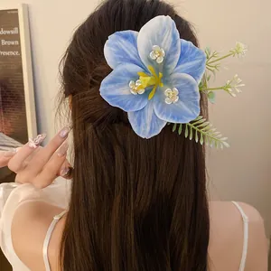 Close-up of a large blue lily floral hair clip accessory styled on long wavy brown hair