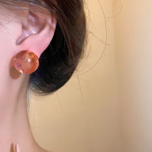 Detailed close-up view of a translucent orange round resin stud earring worn on a female ear