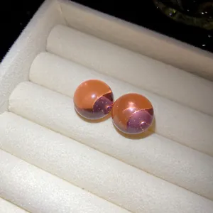 Close-up of translucent dual-tone resin round stud earrings in white velvet box