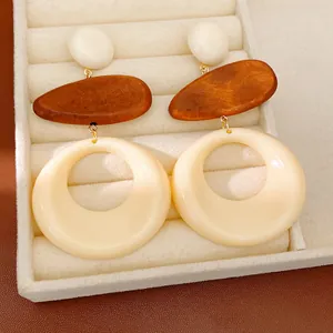 Close-up of geometric drop earrings with wood and cream resin circles in a jewelry tray.
