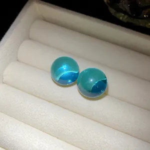 Detailed view of translucent turquoise resin sphere earrings displayed in a white jewelry box.