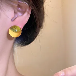 Detail shot of a minimalist round resin stud earring with golden metallic finish.