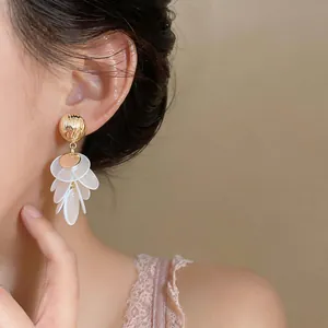 Close-up of elegant French retro gold earrings with white shell petal tassels on a model.