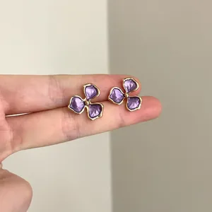 Detailed macro view of purple floral stud earrings with gold trim on fingers