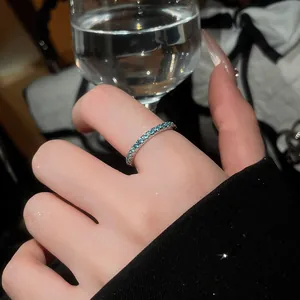 Macro view of a thin mint green zircon row ring on model finger with an elegant glass backdrop