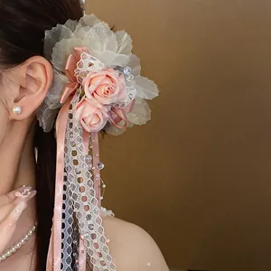 Detail view of a pink lace flower hair clip with dangling ribbons worn on model's hair
