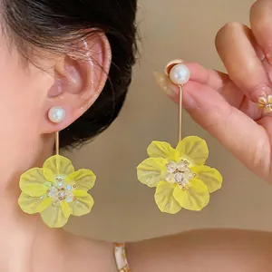 Close-up of elegant long earrings with a white pearl and yellow flower drop