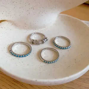 Close-up of four silver rings with mint green zircons and sparkling charms on a ceramic tray.