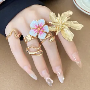 Dettaglio di anelli a fiore 3D dorati con smalto bianco e rosa indossati sulla mano