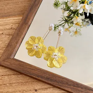 Detailed macro shot of yellow floral earrings with pearls on a mirror surface