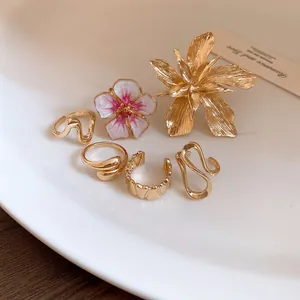 Dettaglio ravvicinato di vari anelli dorati con fiori 3D e anelli aperti minimalisti