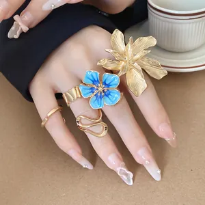 Dettaglio del fiore 3D dorato e degli anelli floreali in smalto blu al dito